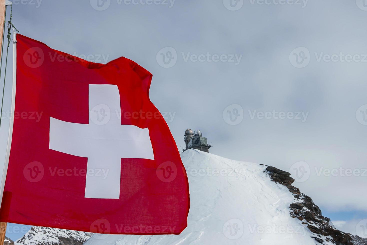 Suisse drapeau agitant contre jungfrau la glace palais sur Haut de neigeux Montagne photo
