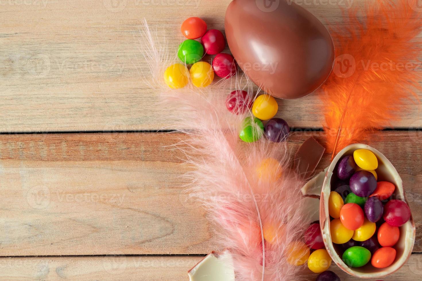 plumes colorées et bonbons de Pâques. oeufs en chocolat pour des vacances sur un fond en bois. photo