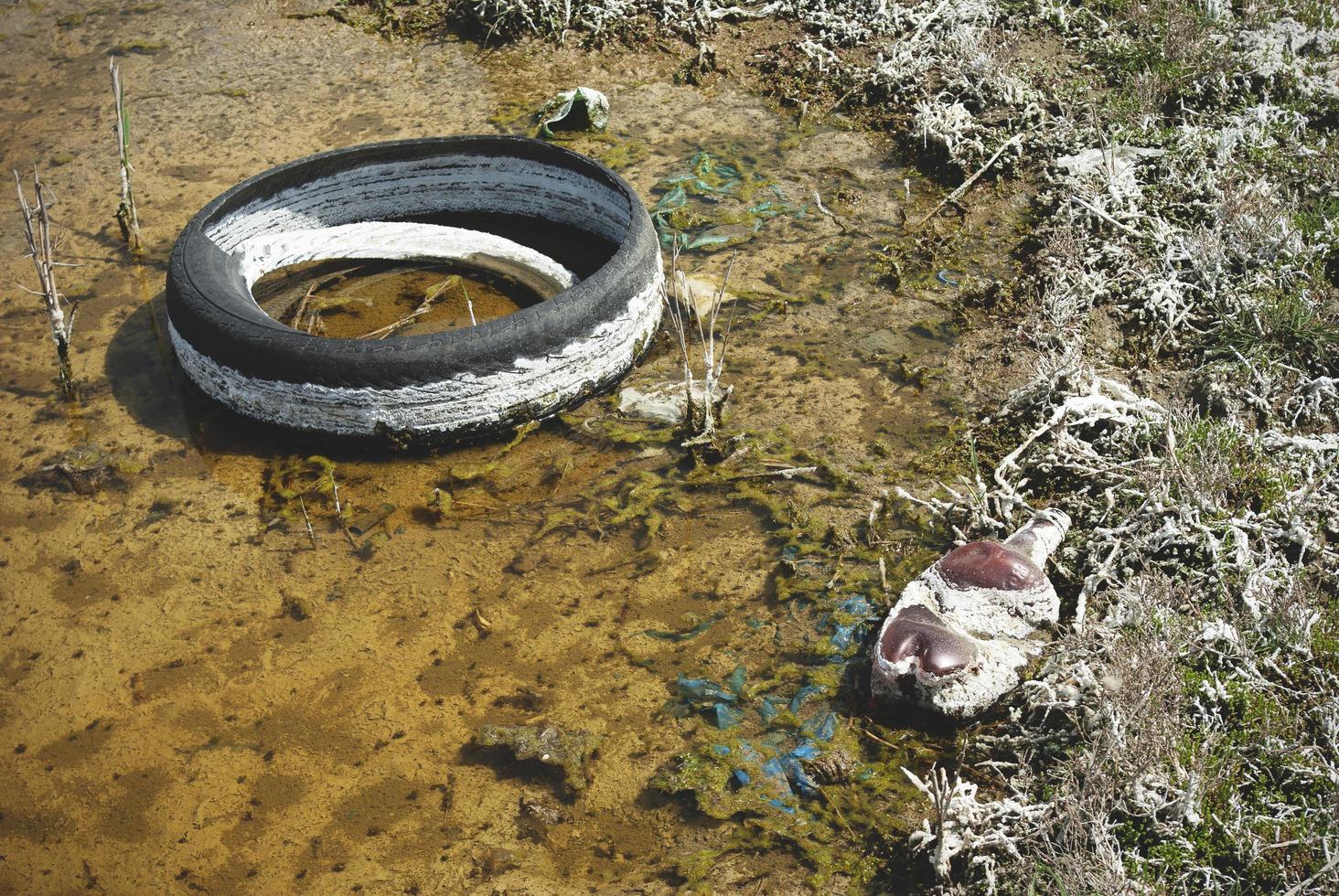 un pneu jeté dans une flaque d'eau. une flaque d'eau polluée par des produits chimiques et des ordures. photo