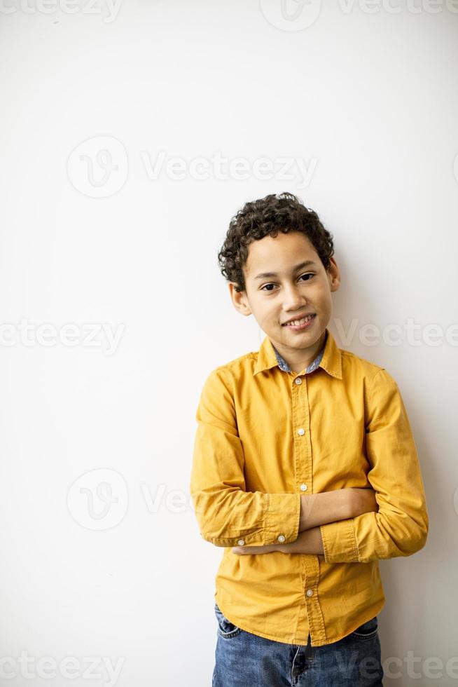 mignon petit garçon aux cheveux bouclés debout près du mur blanc photo