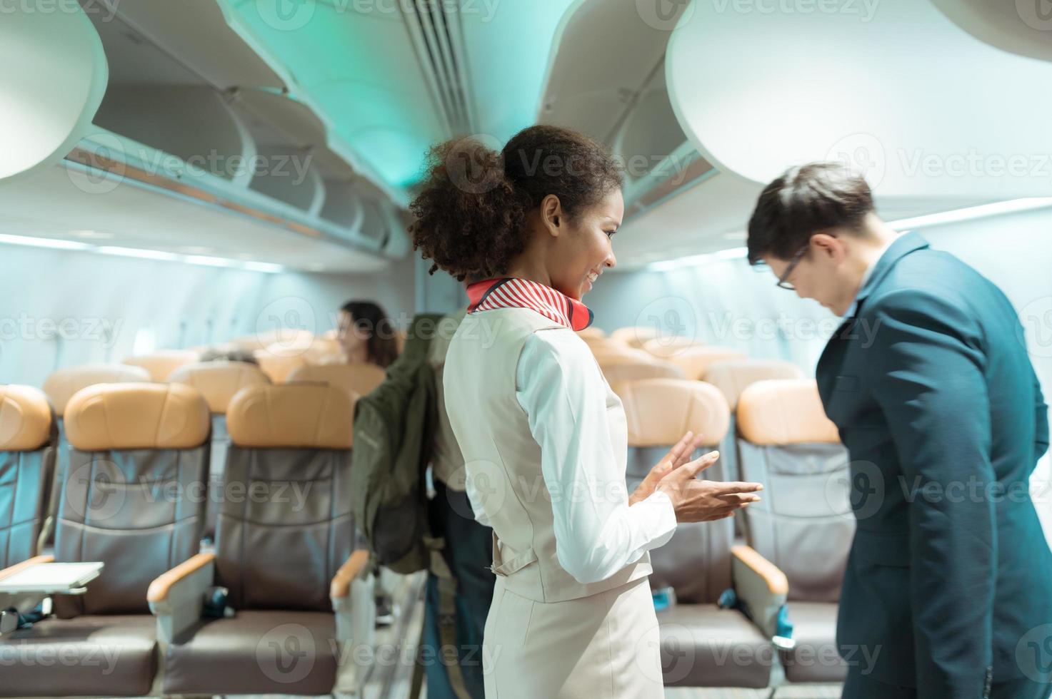 vol préposé saluer les passagers comme elles ou ils entrer le avion à Localiser une siège dans le cabine. photo