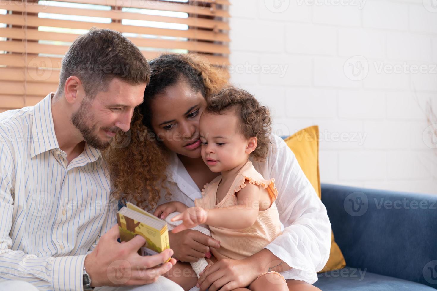 Parents et les enfants se détendre dans le vivant pièce de le maison. regarder bébé Heureusement jouer avec le sien préféré jouet. photo