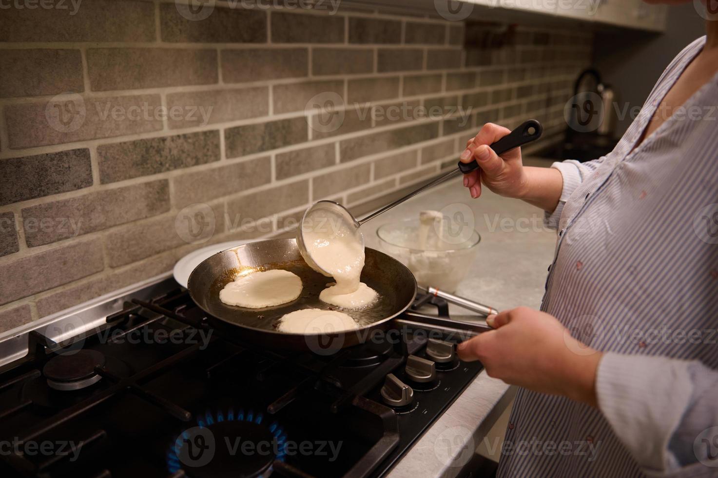 fermer de une femelle chef, femme au foyer, verser Rond Battre dans une friture la poêle plus de une noir le fourneau et en train de préparer Crêpes pour mardi gras. cuisson, rétrécir Mardi, Maslenitsa concept photo