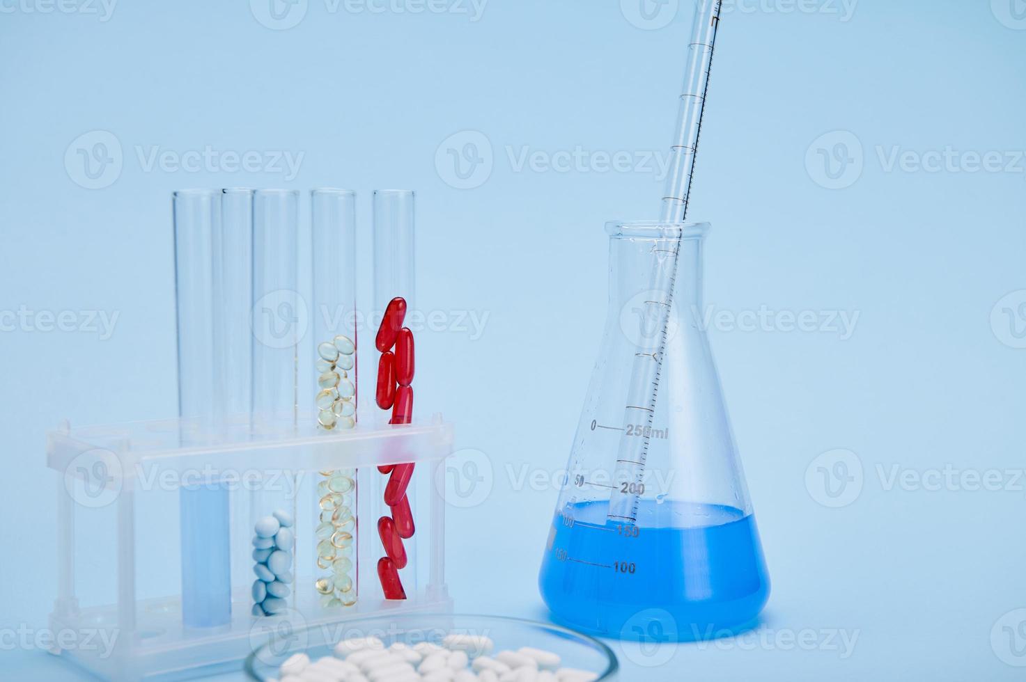 tester tubes avec Gélatine gélules, pétri plat avec pilules et diplômé pipette à l'intérieur une laboratoire ballon avec fluide Solution photo