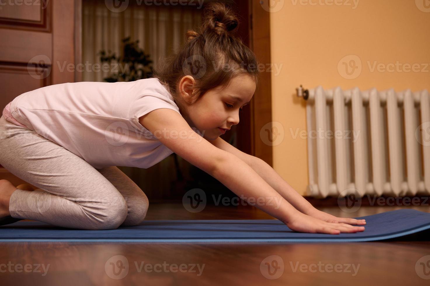 fermer peu fille élongation sa corps dans balasana pose, séance dans enfant pose tandis que pratiquant yoga sur une aptitude tapis photo