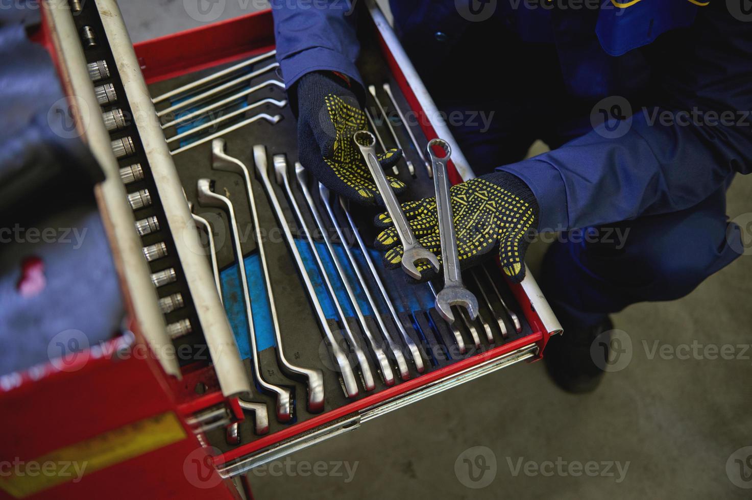 aérien vue de une mécanicien en portant clés au dessus une ensemble de outils de clés et têtes pour dévisser des noisettes et boulons dans une spécial cabinet pour réparation dans une voiture service. industrie et fabrication. photo