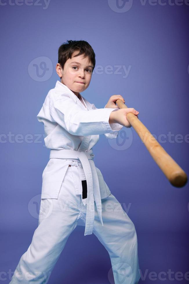 concentré garçon - aikido lutteur dans une kimono pratiquant combat compétences avec en bois jo arme dans le sien mains. Oriental martial les arts entraine toi concept photo