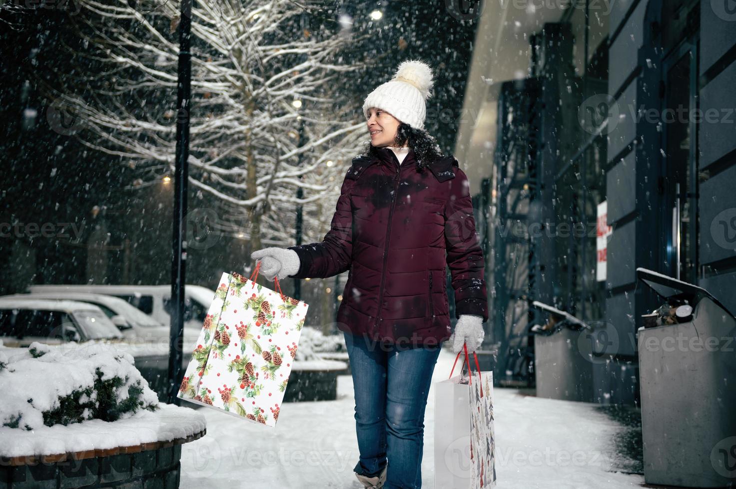 délicieux Jeune femme en marchant vers le bas le rue avec achats Sacs avec Noël cadeau boîte dans sa mains. joyeux Noël. photo