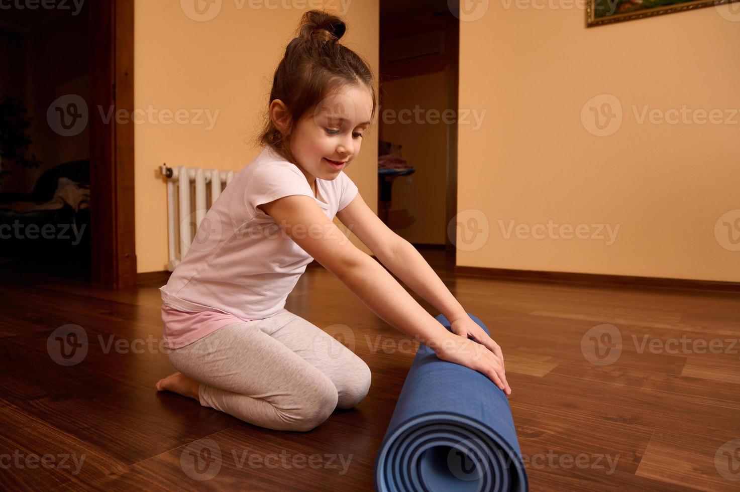 plein longueur charmant enfant d'âge préscolaire enfant fille séance pieds nus sur une en bois sol et pliant yoga tapis après aptitude à Accueil photo