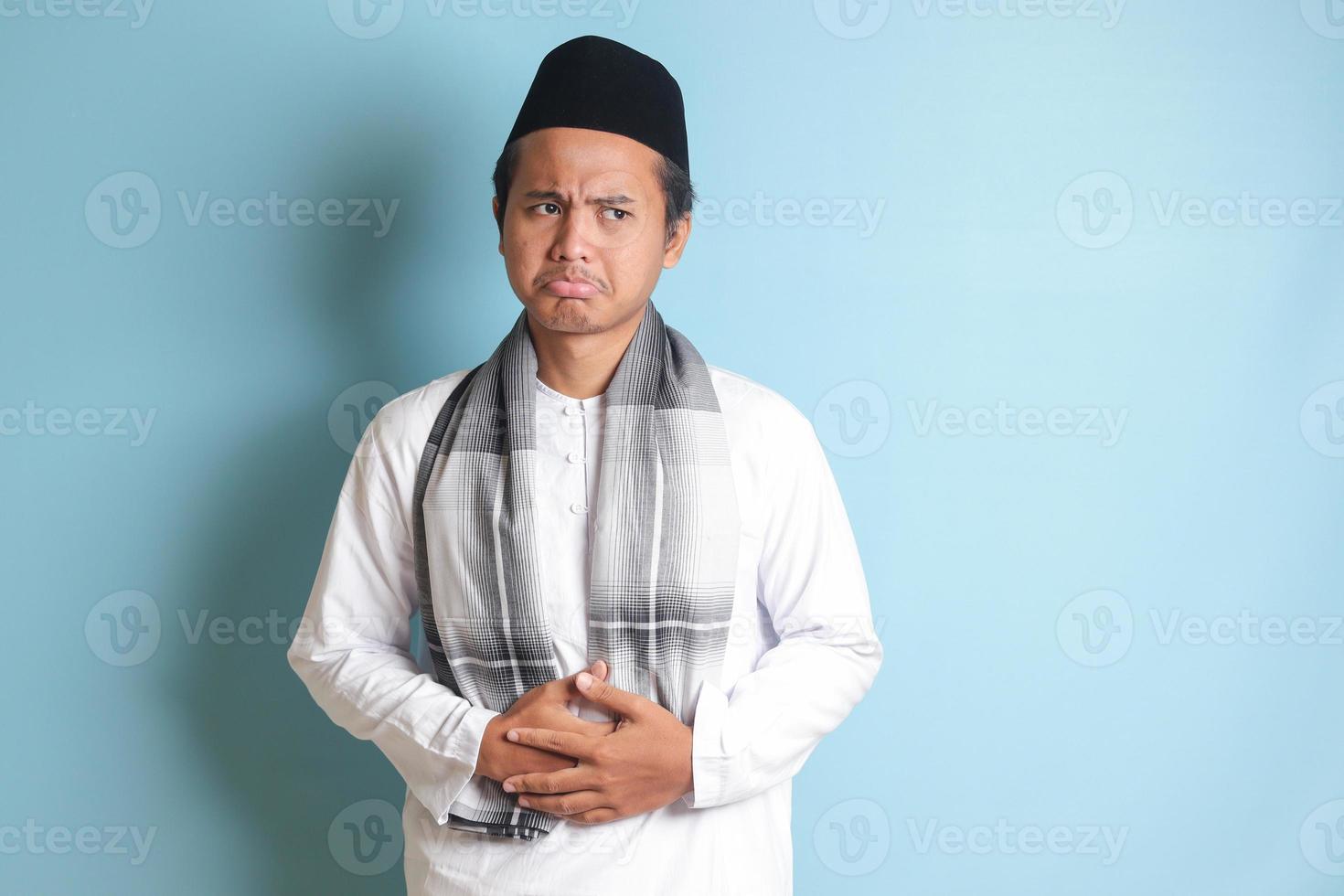 portrait de Jeune asiatique musulman homme sentiment douleur dans le sien estomac. maux d'estomac concept. isolé image sur bleu Contexte photo