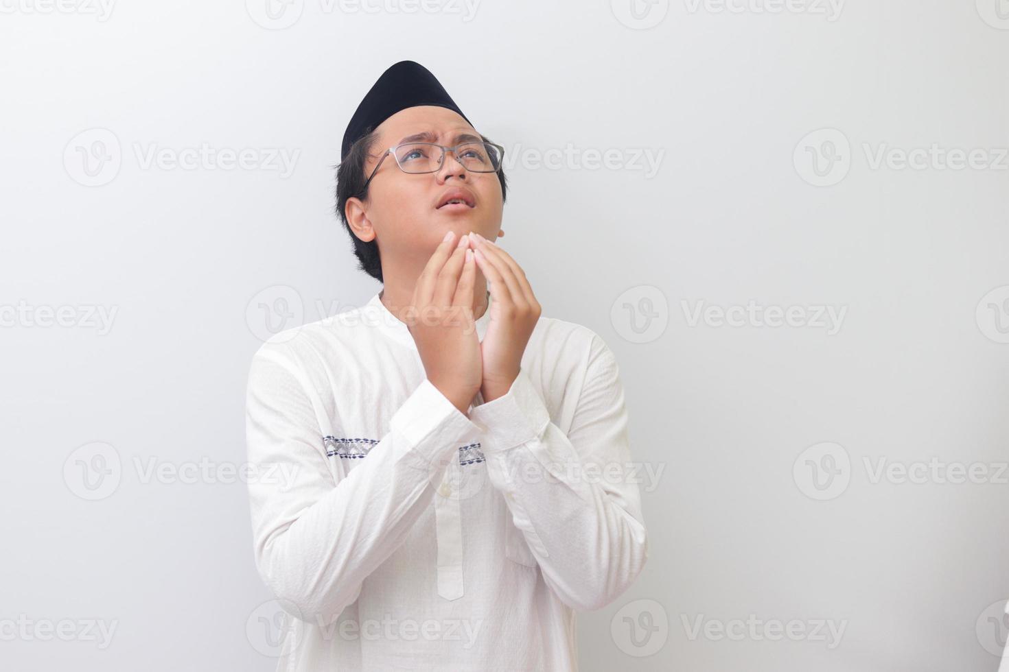 portrait de Jeune millénaire asiatique musulman homme prier sérieusement avec le sien mains soulevé. isolé image sur blanc Contexte photo