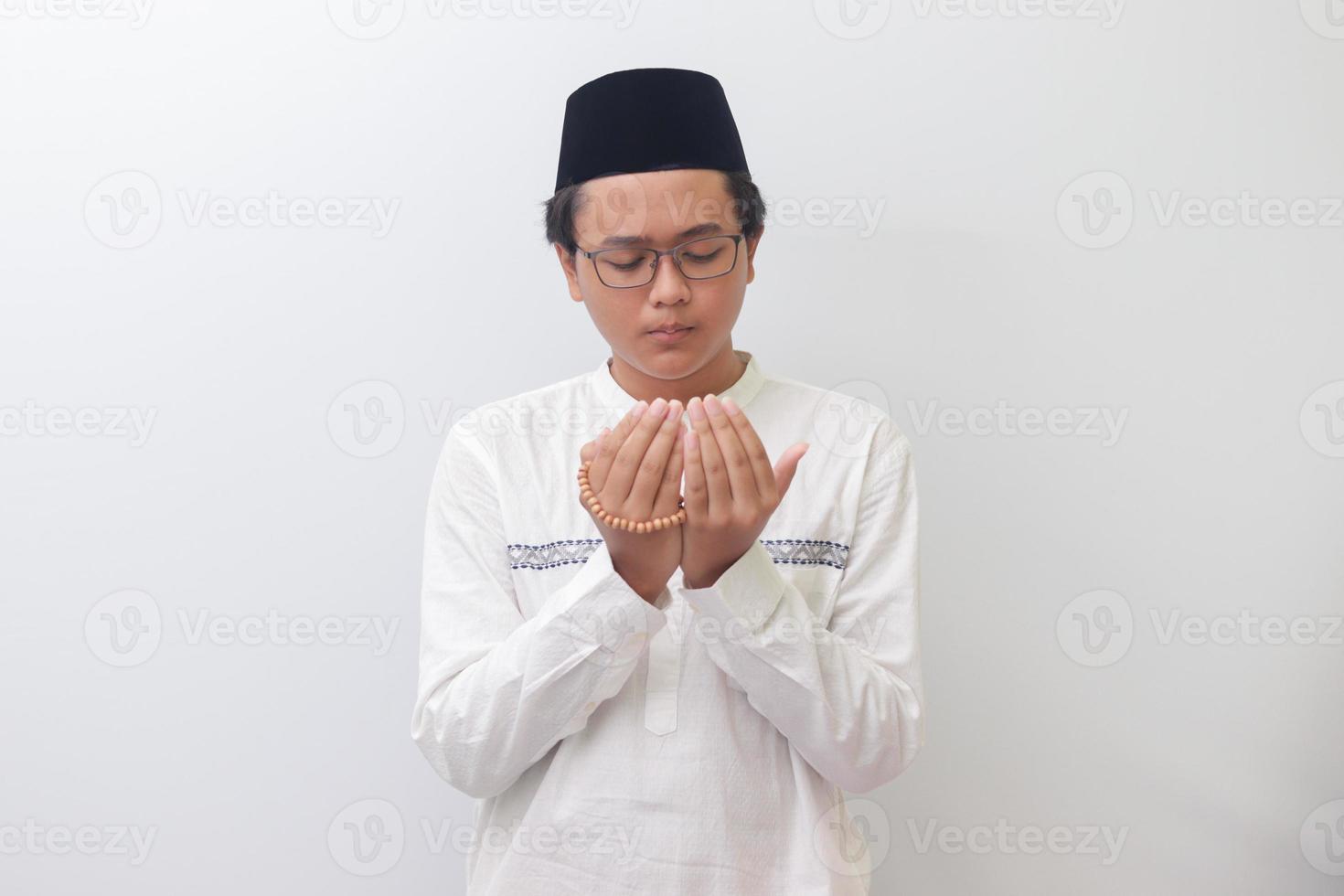 portrait de Jeune millénaire asiatique musulman homme prier sérieusement avec le sien mains soulevé. isolé image sur blanc Contexte photo