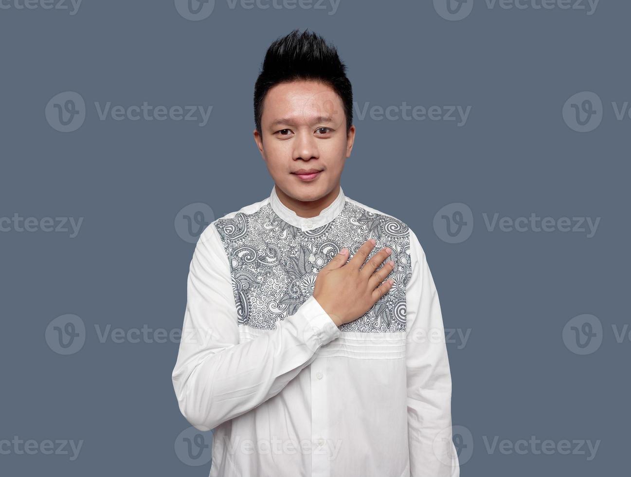 indonésien homme portant koko chemise mains sur le sien poitrine avec Bienvenue main salutation photo