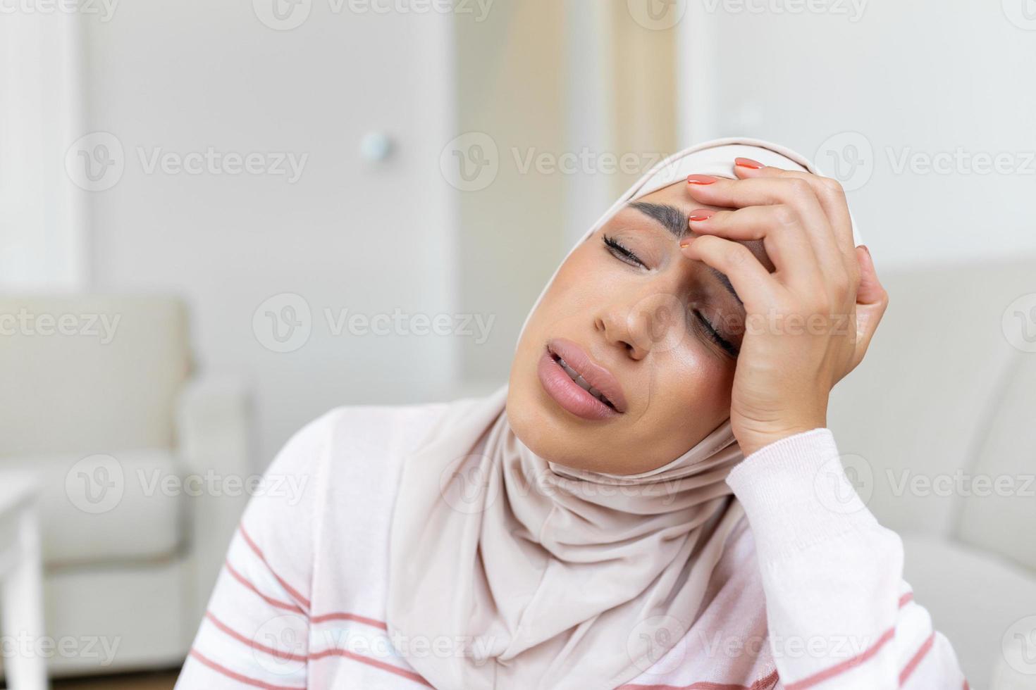 portrait de un arabe musulman femme séance sur une canapé à Accueil avec une mal de tête, sentiment douleur et avec un expression de étant indisposé. dérangé femme mensonge sur canapé sentiment fort mal de crâne migraine. photo