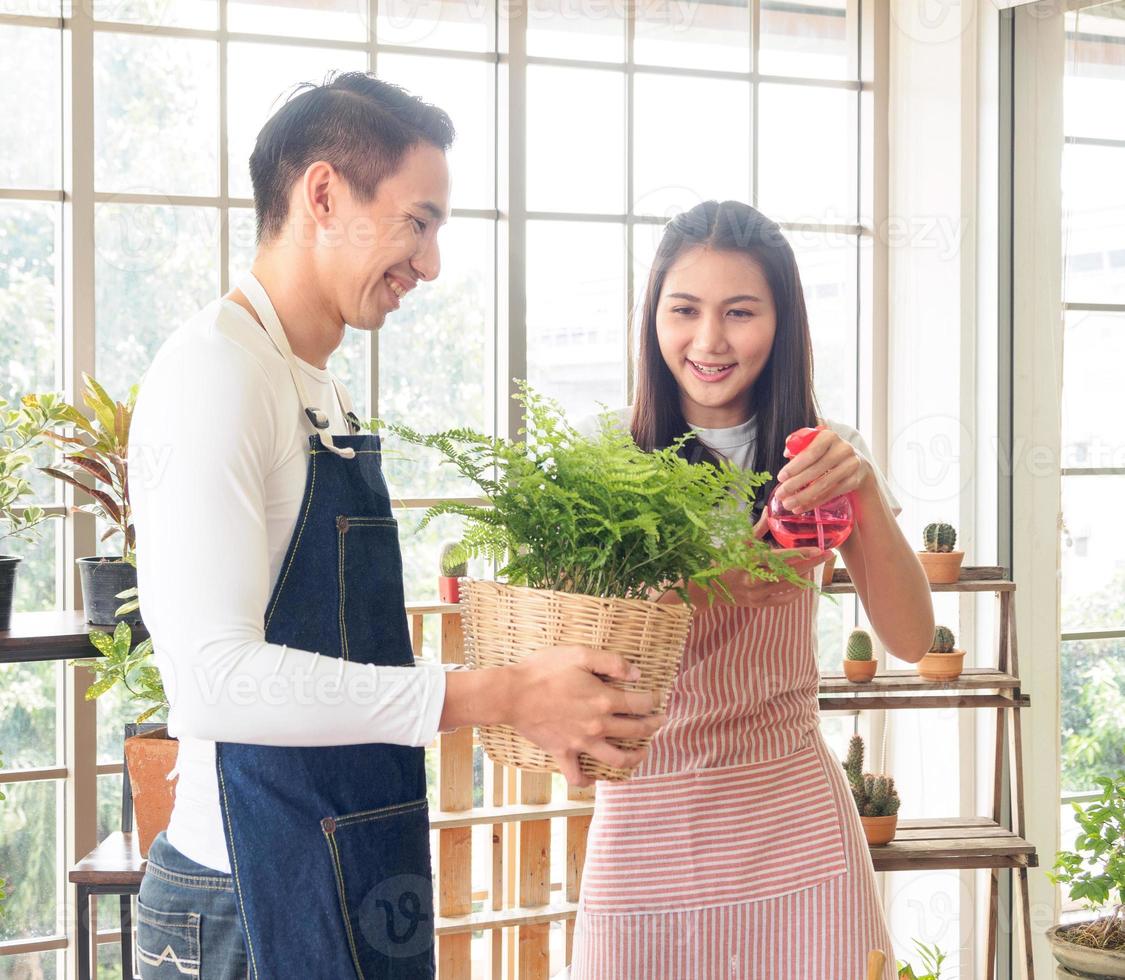 portrait les amoureux Beau Jeune homme jolie asiatique femme portant blanc T-shirt. et tablier plaisanterie ayant amusement Aidez-moi organiser plante et l'eau les plantes dans petit des pots dans le pièce arrangé les plantes avec l'amour Heureusement photo