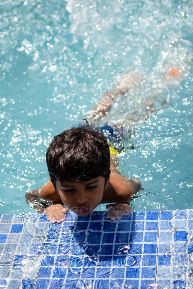 content Indien garçon nager dans une piscine, enfant portant nager costume le long de avec air tube pendant chaud été les vacances, les enfants garçon dans gros nager bassin. photo