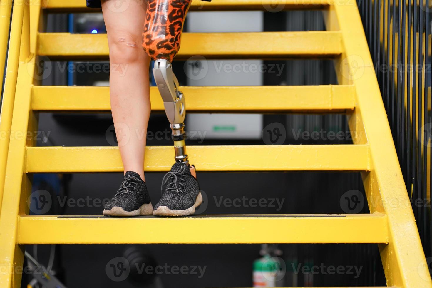 Jeune femelle avec un prothétique jambe avec formation à marcher en haut et vers le bas escaliers à entraine toi le mixte utilisation de prothèses brin Ordinaire jambes, concept de la vie de femmes avec prothèses photo