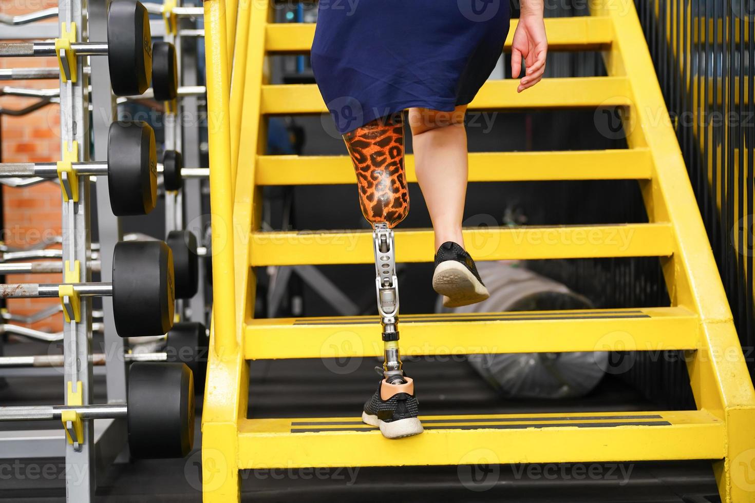 Jeune femelle avec un prothétique jambe avec formation à marcher en haut et vers le bas escaliers à entraine toi le mixte utilisation de prothèses brin Ordinaire jambes, concept de la vie de femmes avec prothèses photo