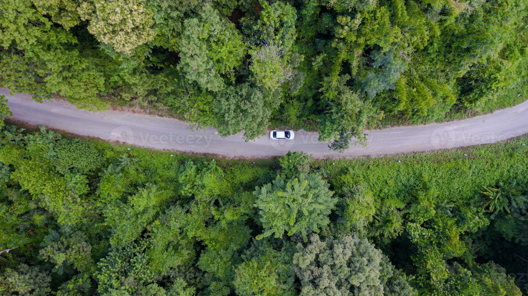 Vue de dessus aérienne voiture roulant à travers la forêt sur route de campagne, vue depuis un drone photo