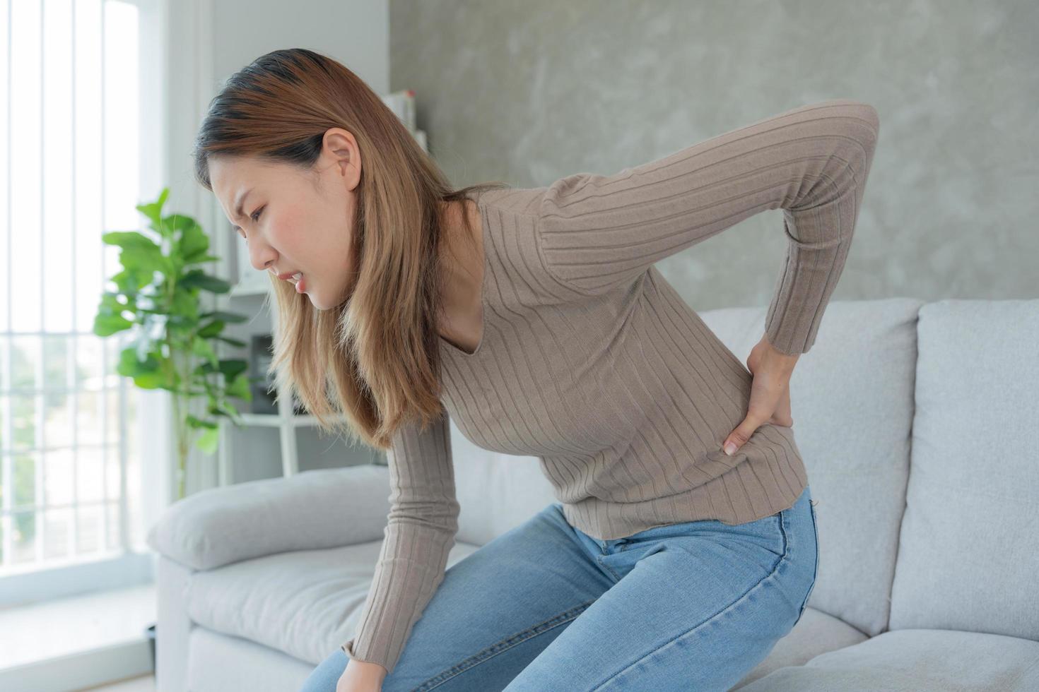 Asie magnifique femme en portant sa inférieur retour tandis que et Souffrance de insupportable douleur santé et problèmes, chronique retour douleur, mal au dos dans Bureau syndrome, scoliose, hernie disque, muscle inflammation photo