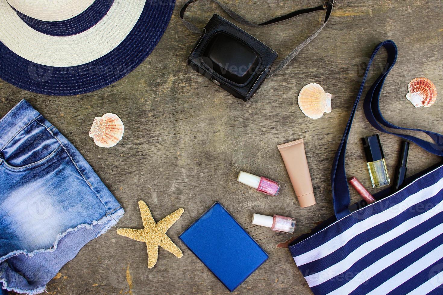 plage sac, Soleil chapeau, produits de beauté, denim shorts, caméra, coquillages sur vieux en bois Contexte. photo