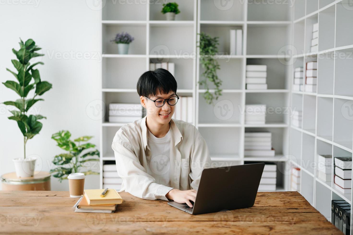 Beau et talentueux Jeune asiatique homme étudiant travail sur le sien projet mission, en utilisant portable et tablette à chercher un en ligne informations. photo