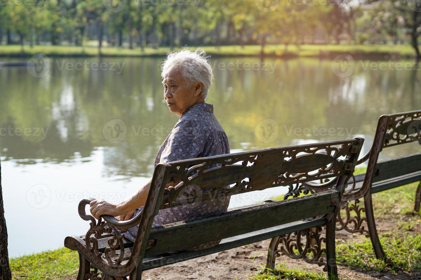 femme âgée asiatique déprimée et triste assise sur un banc dans le parc d'automne. photo
