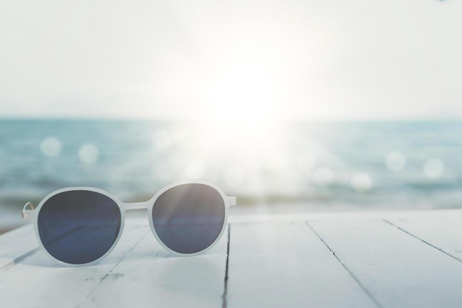 mise au point sélective des lunettes de soleil sur la table à la station balnéaire d'été avec fond de lumière du soleil. tourisme de voyage de vacances de vacances. photo