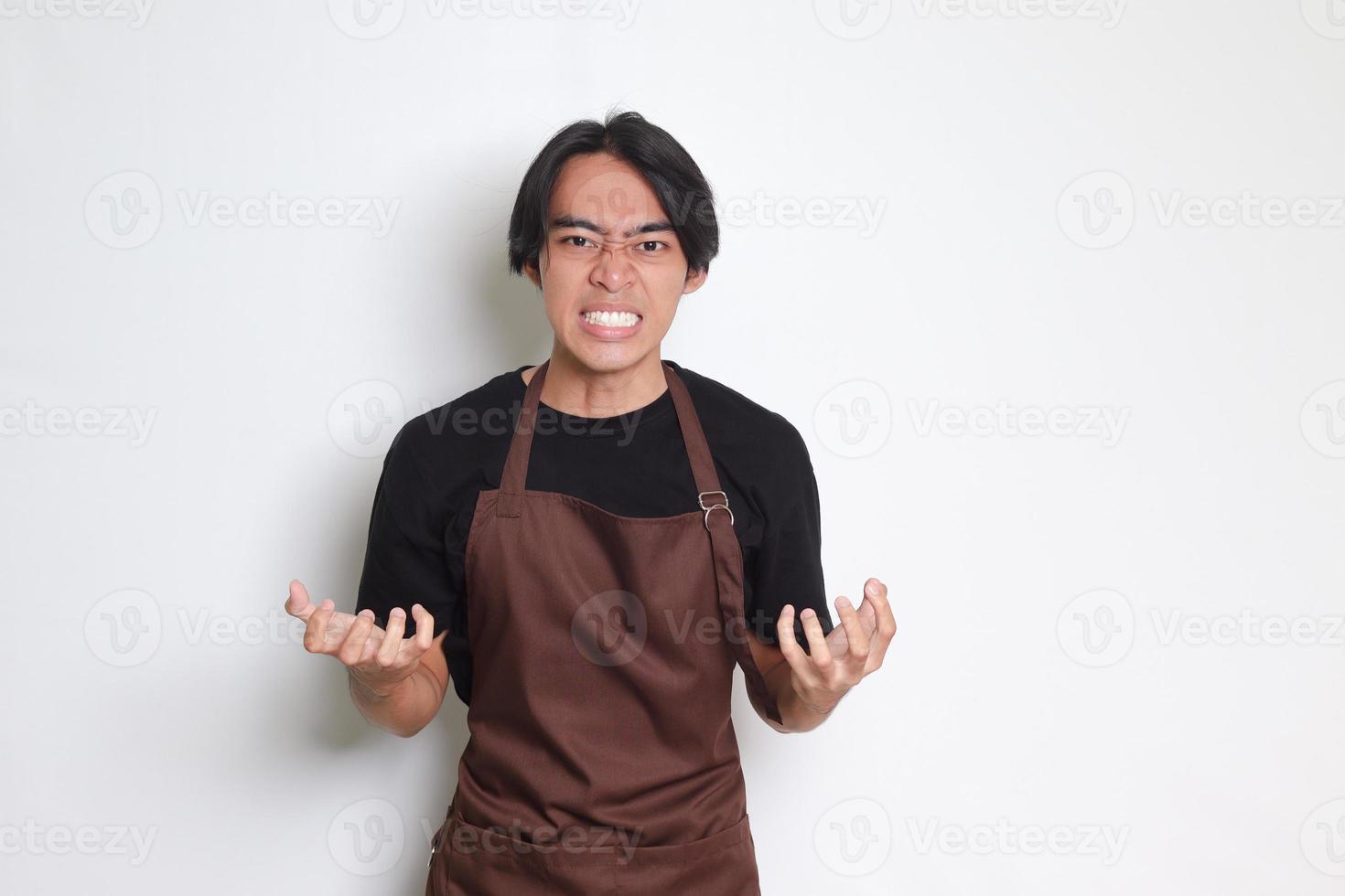 portrait de agacé asiatique barista homme dans marron tablier fabrication en colère main geste avec des doigts. isolé image sur blanc Contexte photo