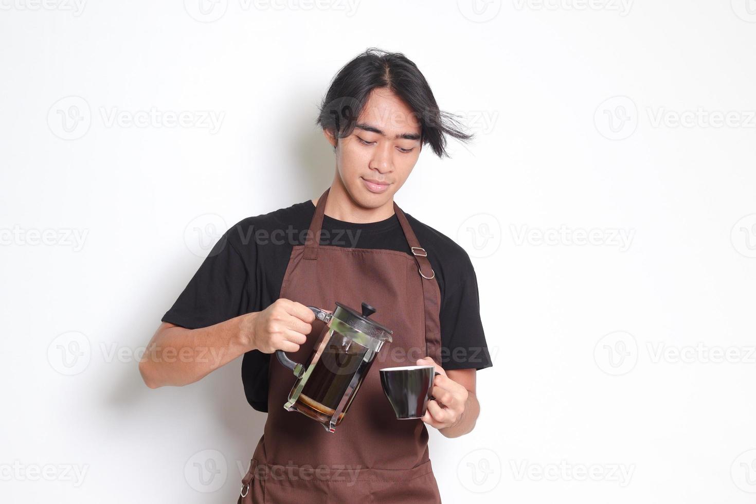 portrait de attrayant asiatique barista homme dans marron tablier verser café dans une tasse de français presse café fabricant. isolé image sur blanc Contexte photo