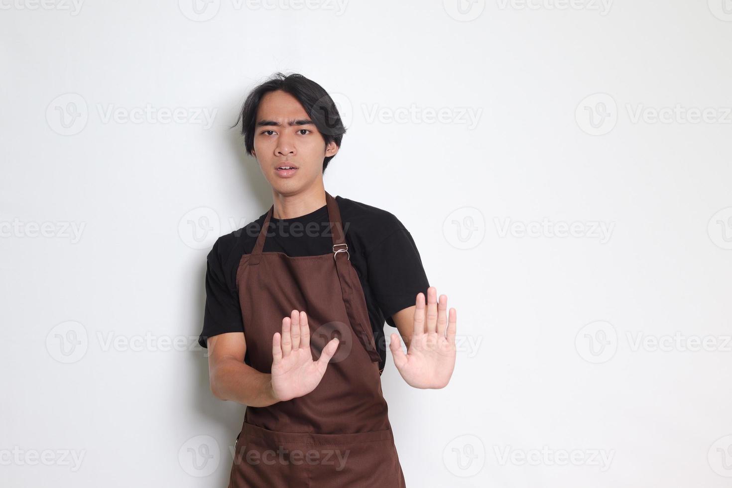 portrait de attrayant asiatique barista homme dans marron tablier formant une main geste à éviter quelque chose. isolé image sur blanc Contexte photo