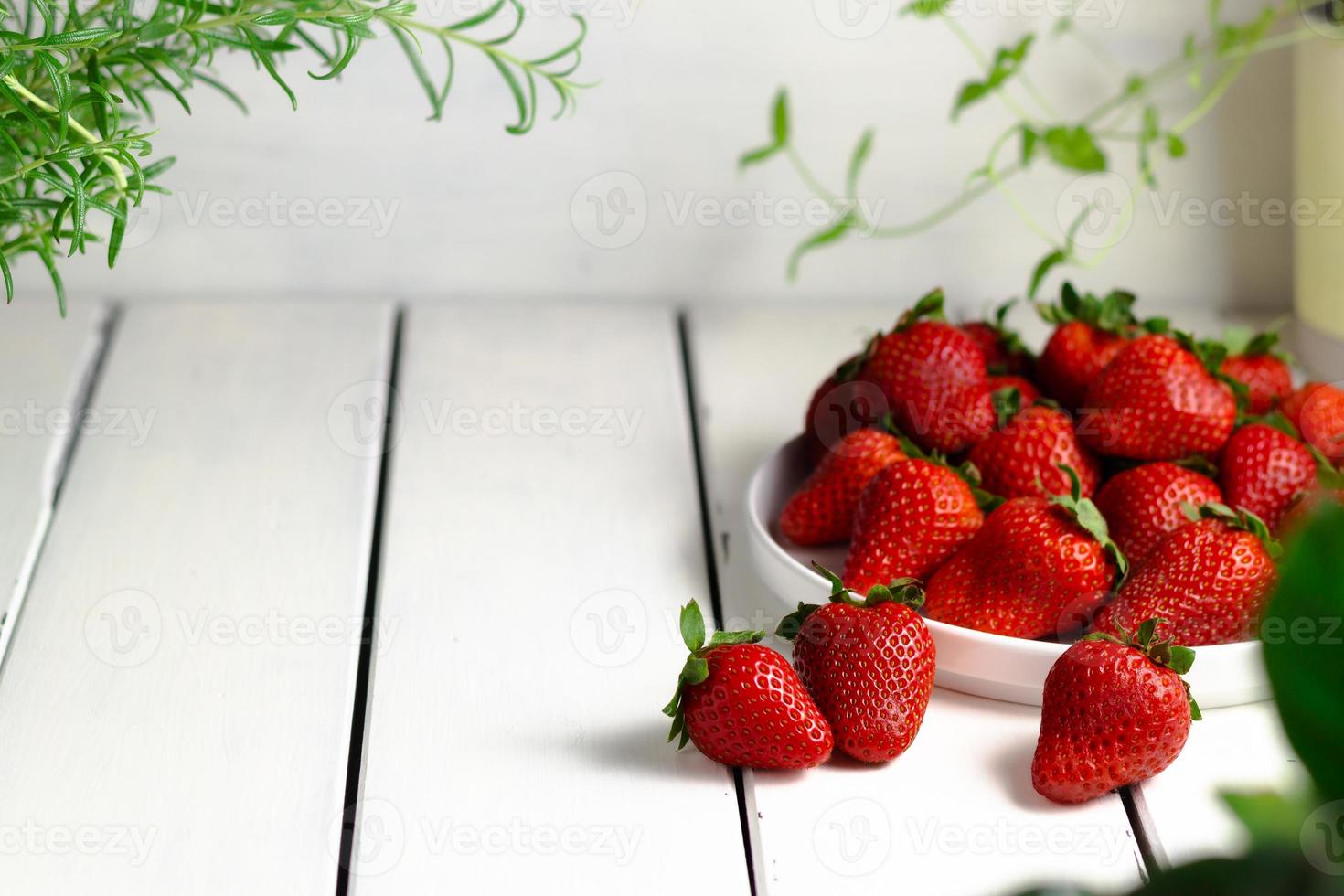 tas de Frais des fraises dans céramique bol sur rustique blanc en bois Contexte. photo