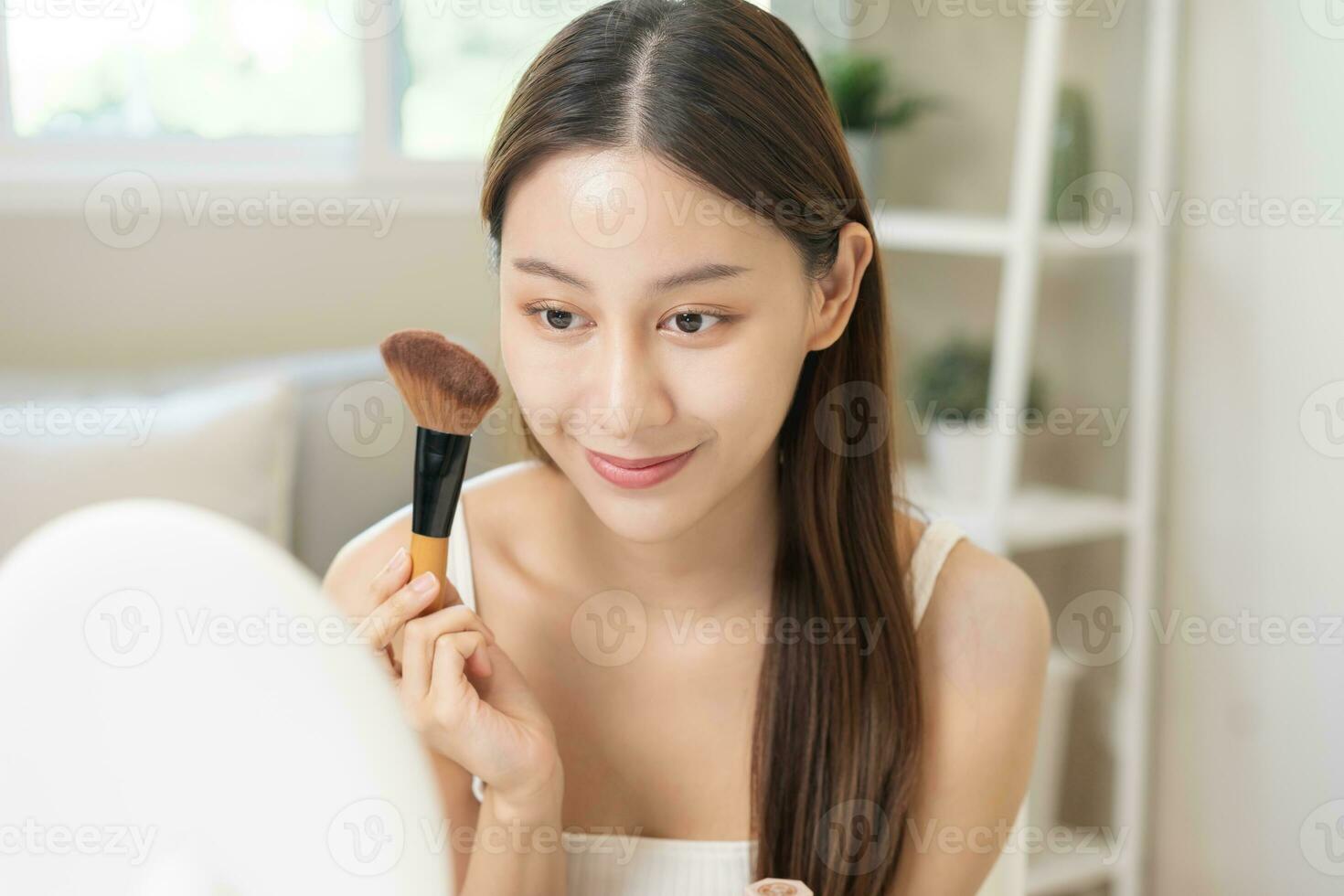 content beauté blogueur concept, mignonne asiatique Jeune femme, fille sourire, faire en haut visage par appliquant brosse rougir poudre sur sa joue, à la recherche à le miroir. gens Regardez avec Naturel mode style. photo