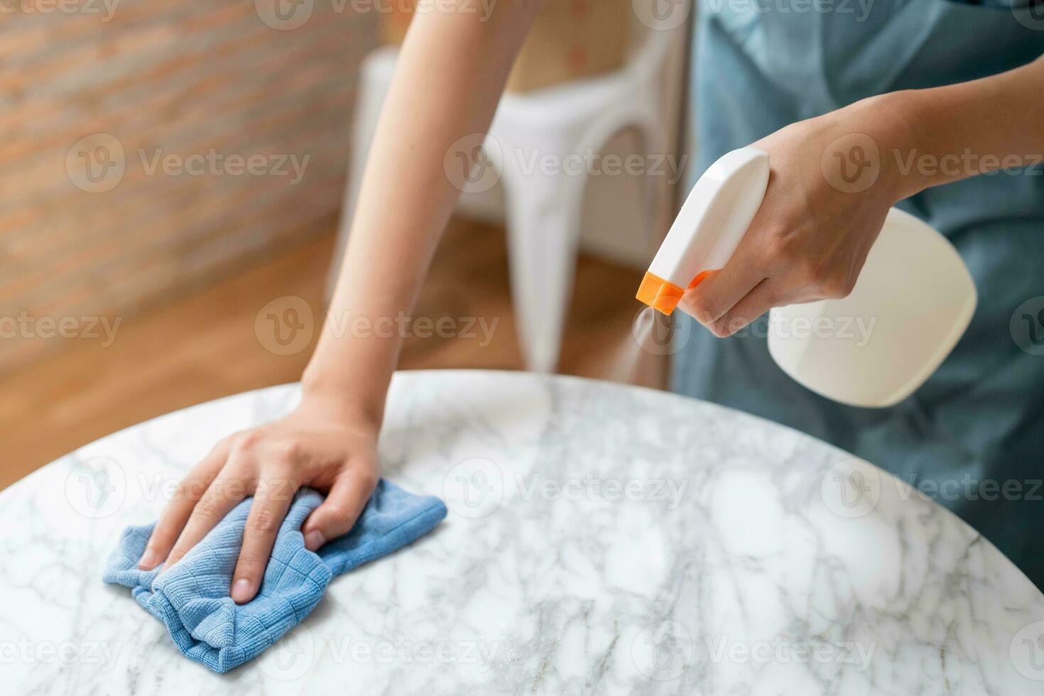 nettoyage hygiène, asiatique Jeune Femme de ménage femme, fille main dans en utilisant une l'eau pulvérisateur bouteille à essuyer faire le ménage, utilisation bleu chiffon essuyage à poussière sur blanc marbre table dans restaurant. Entretien ménager nettoyer, nettoyeur. photo