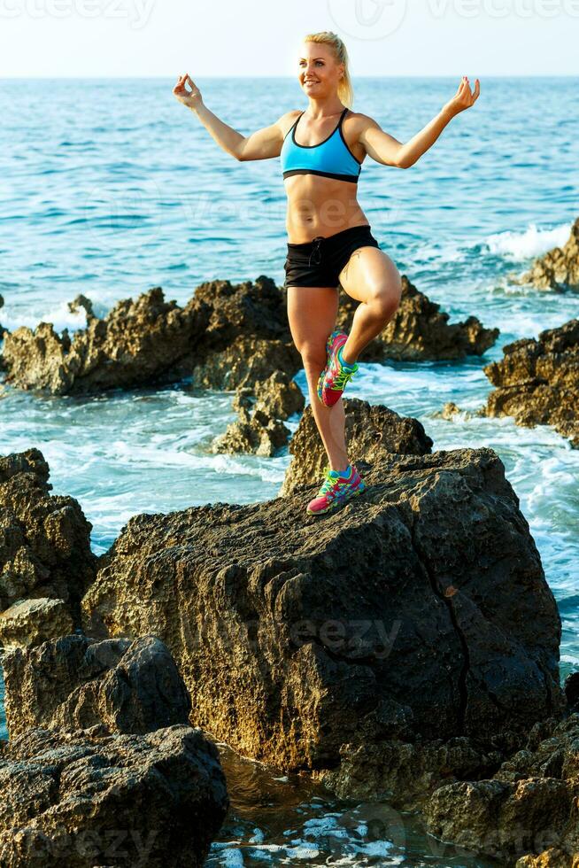 athlétique femme relaxant - pratiquant yoga sur le rochers par le mer photo