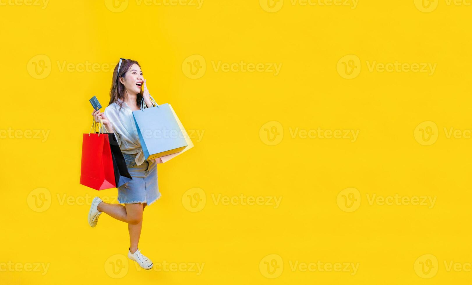 jolie asiatique femme dans branché été mode est souriant et en portant achats sac dans bonheur pour remise vente isolé sur Jaune Contexte pour La publicité et promotion un événement concept photo