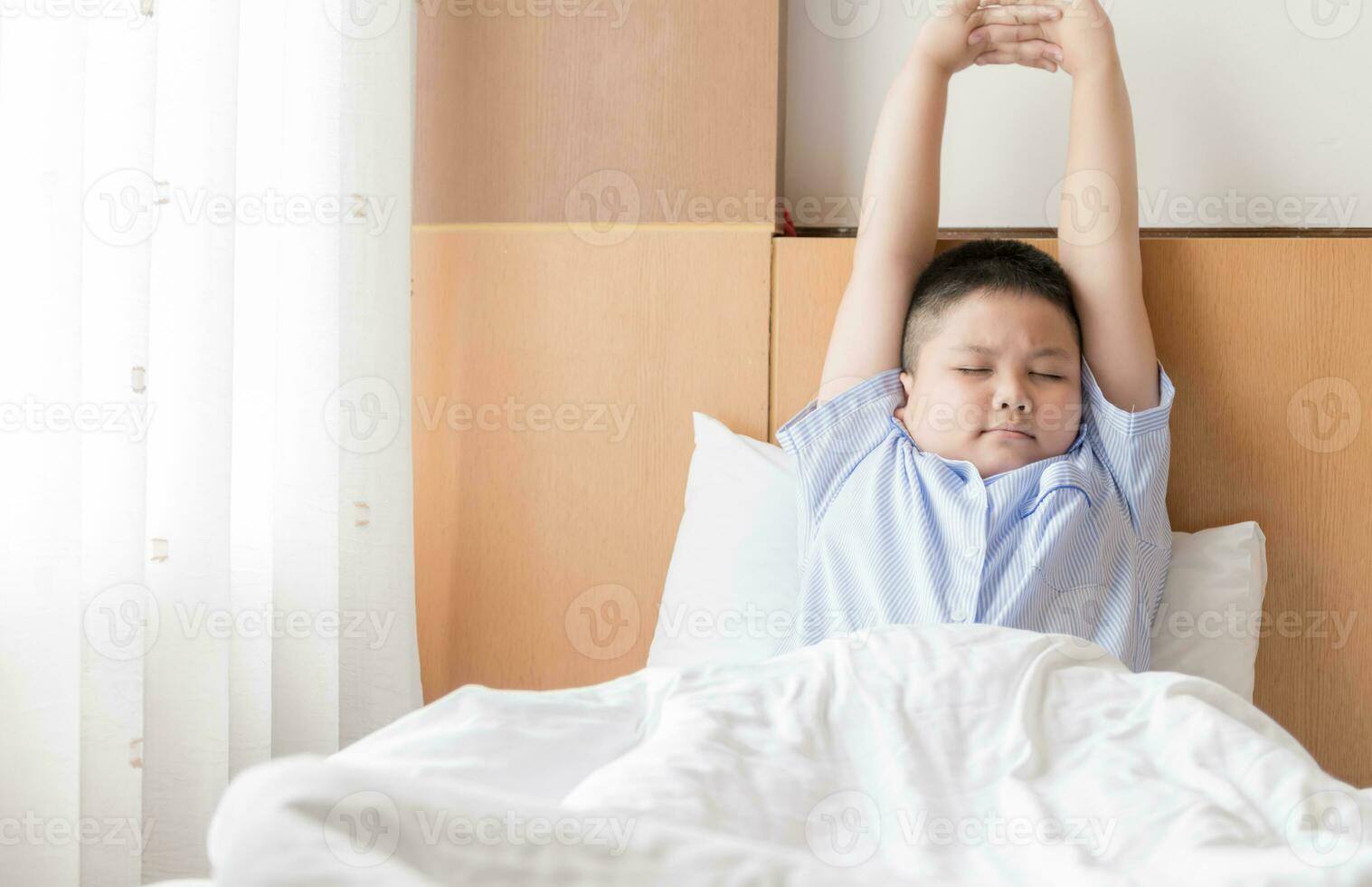 obèse graisse garçon se réveille en haut et élongation sur lit. photo