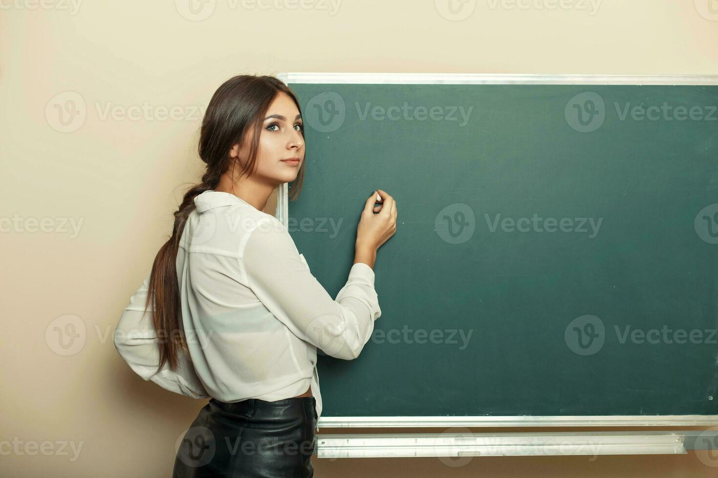 magnifique Jeune fille écrit craie sur le tableau noir. photo