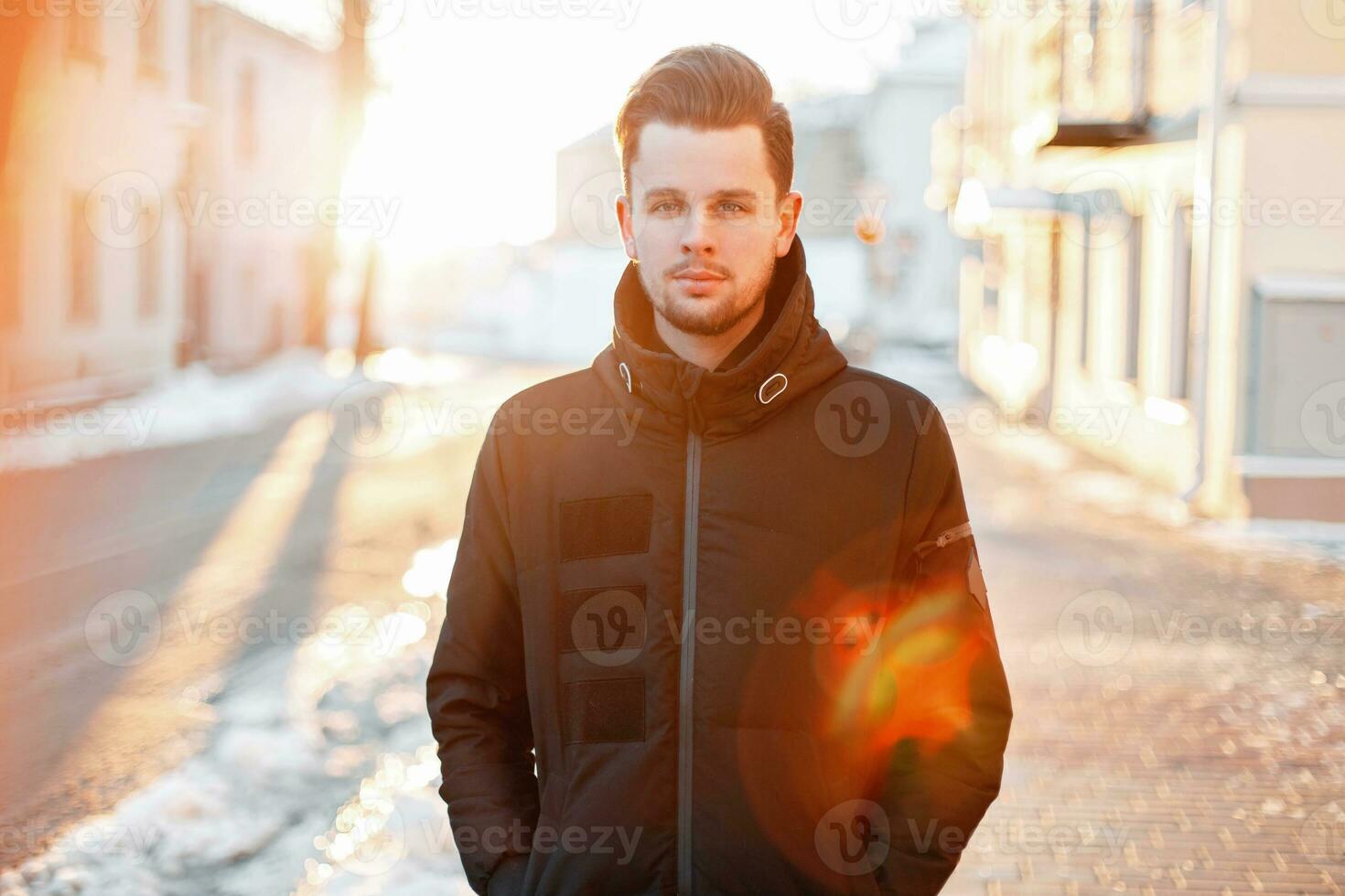 Beau Jeune homme avec cheveux style dans une noir veste en marchant sur le rue à le coucher du soleil photo