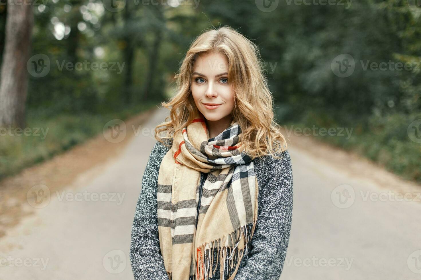 magnifique élégant Jeune femme dans une chaud écharpe et manteau en marchant le long de le route dans le parc photo