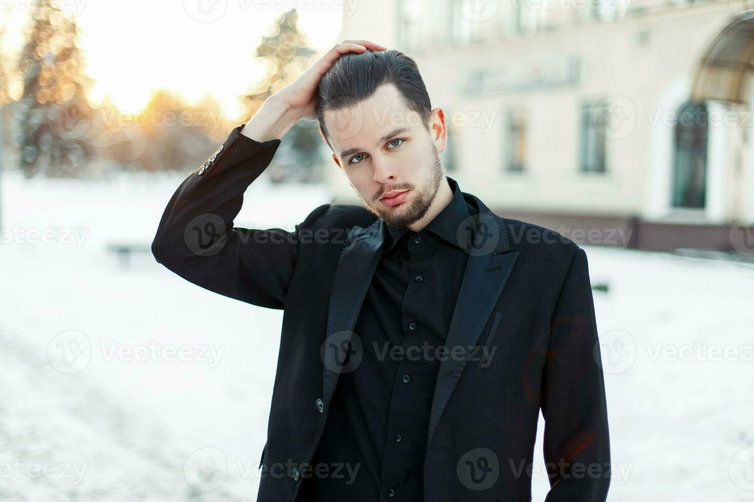 Beau élégant homme dans une noir costume posant sur une neigeux journée à le coucher du soleil photo