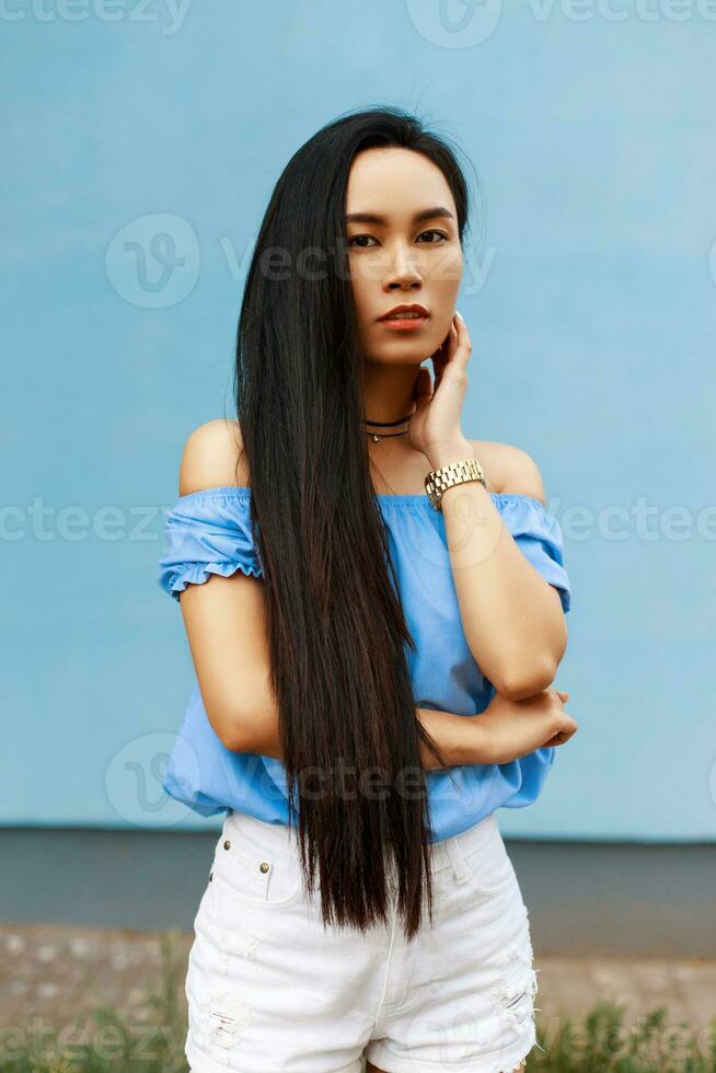 jolie magnifique asiatique femme dans une à la mode été vêtements permanent près une bleu mur photo