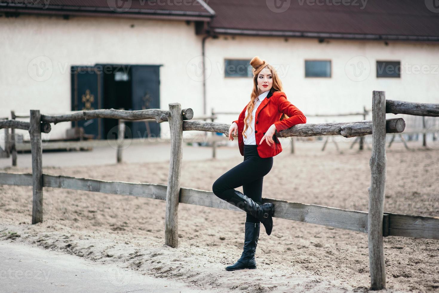 Fille jockey aux cheveux roux dans un cardigan rouge et des bottes hautes noires photo