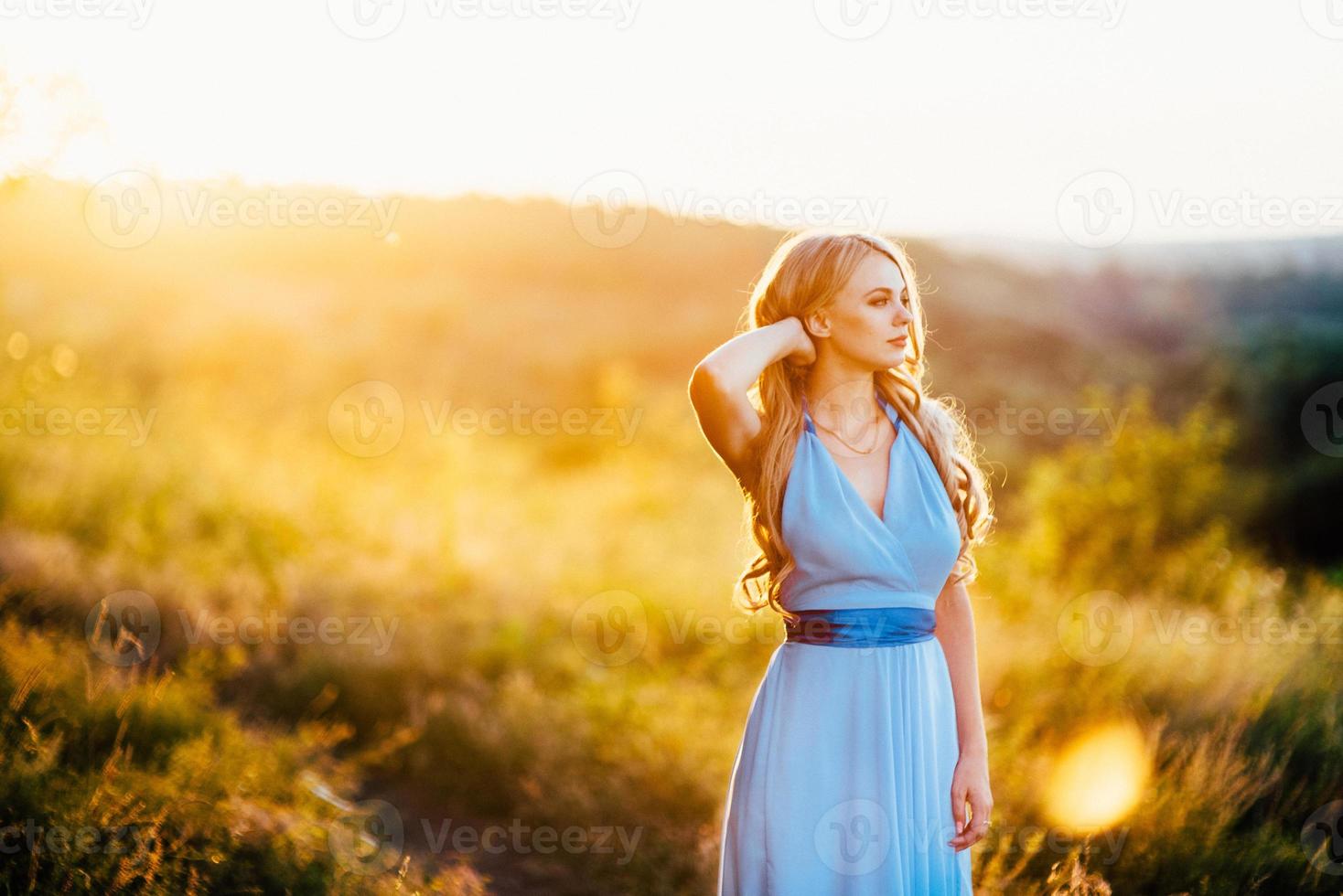 Femme blonde aux cheveux lâches dans une robe bleu clair à la lumière du coucher du soleil photo