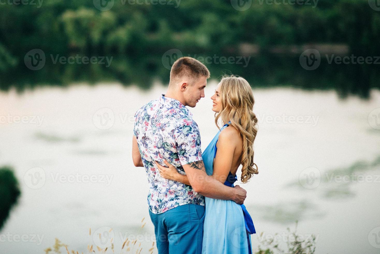 Fille blonde aux cheveux lâches dans une robe bleu clair et un mec à la lumière du coucher du soleil photo