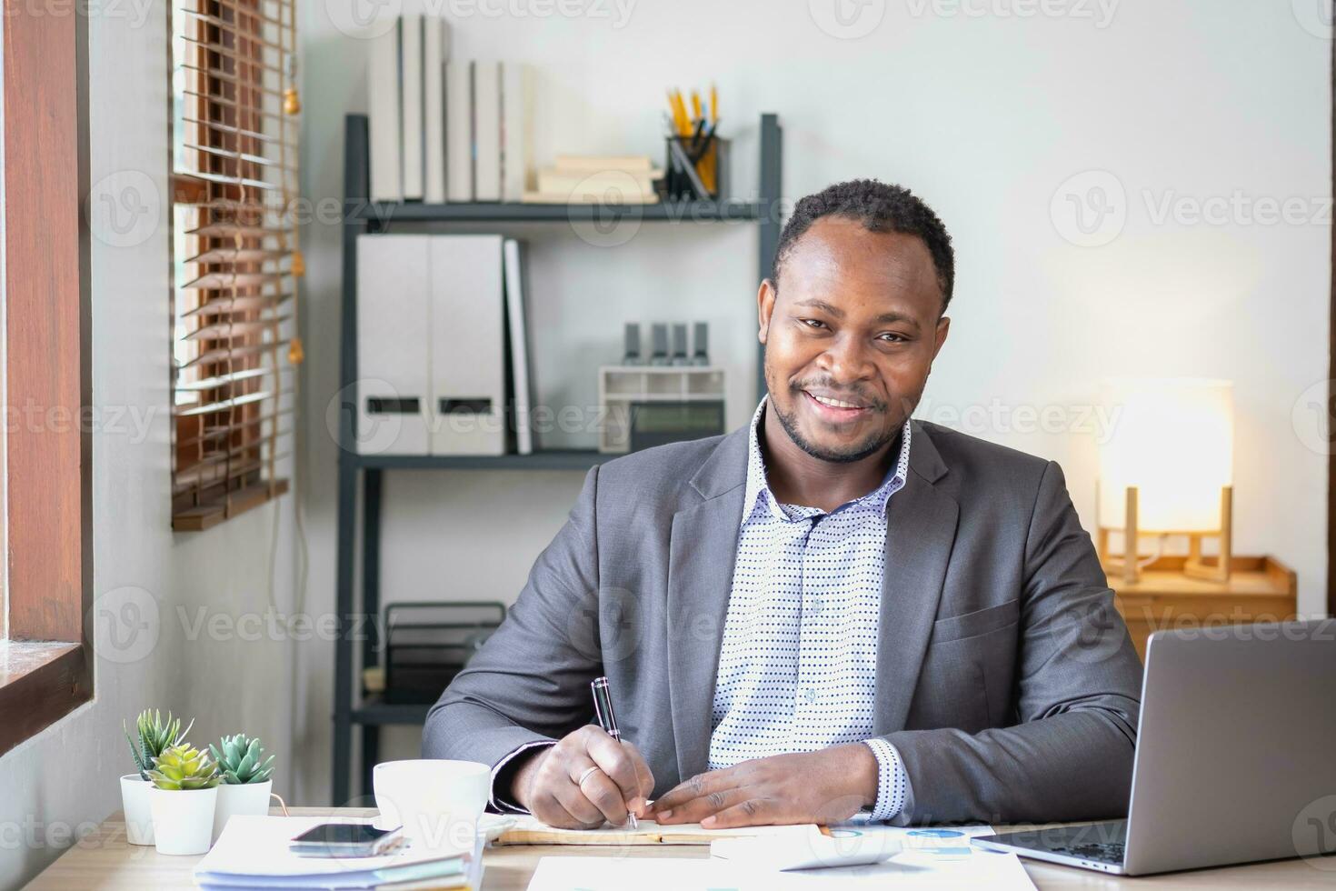 un africain américain homme d'affaire dans une noir costume souriant et montrant joie à le de l'entreprise annuel profit à construire confiance pour les clients qui volonté investir dans le bureau. photo