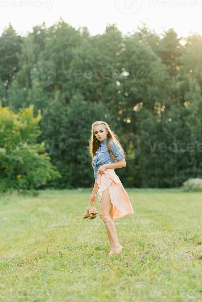 une magnifique Jeune femme détient été des chaussures dans sa mains et des promenades pieds nus sur le herbe sur une été journée photo