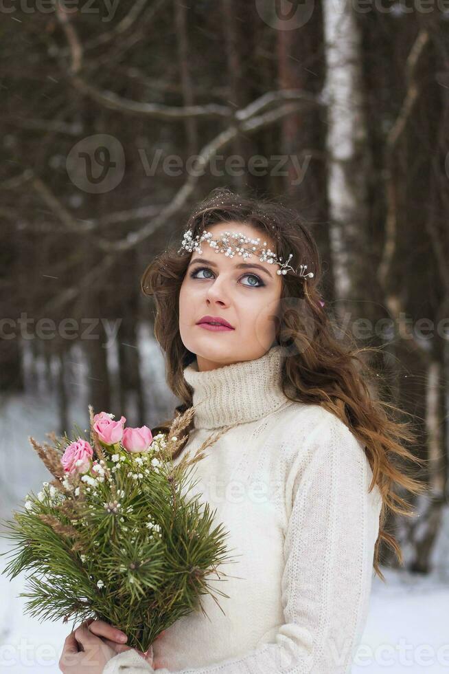 magnifique la mariée dans une blanc robe avec une bouquet dans une couvert de neige hiver forêt. portrait de le la mariée dans la nature. photo