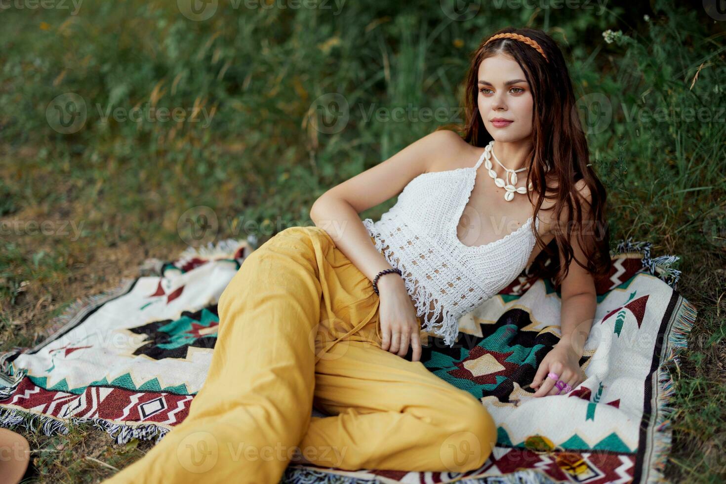 Jeune magnifique hippie femme mensonge sur le sol dans la nature dans le tomber dans éco vêtements dans Jaune un pantalon dans le le coucher du soleil lumière photo