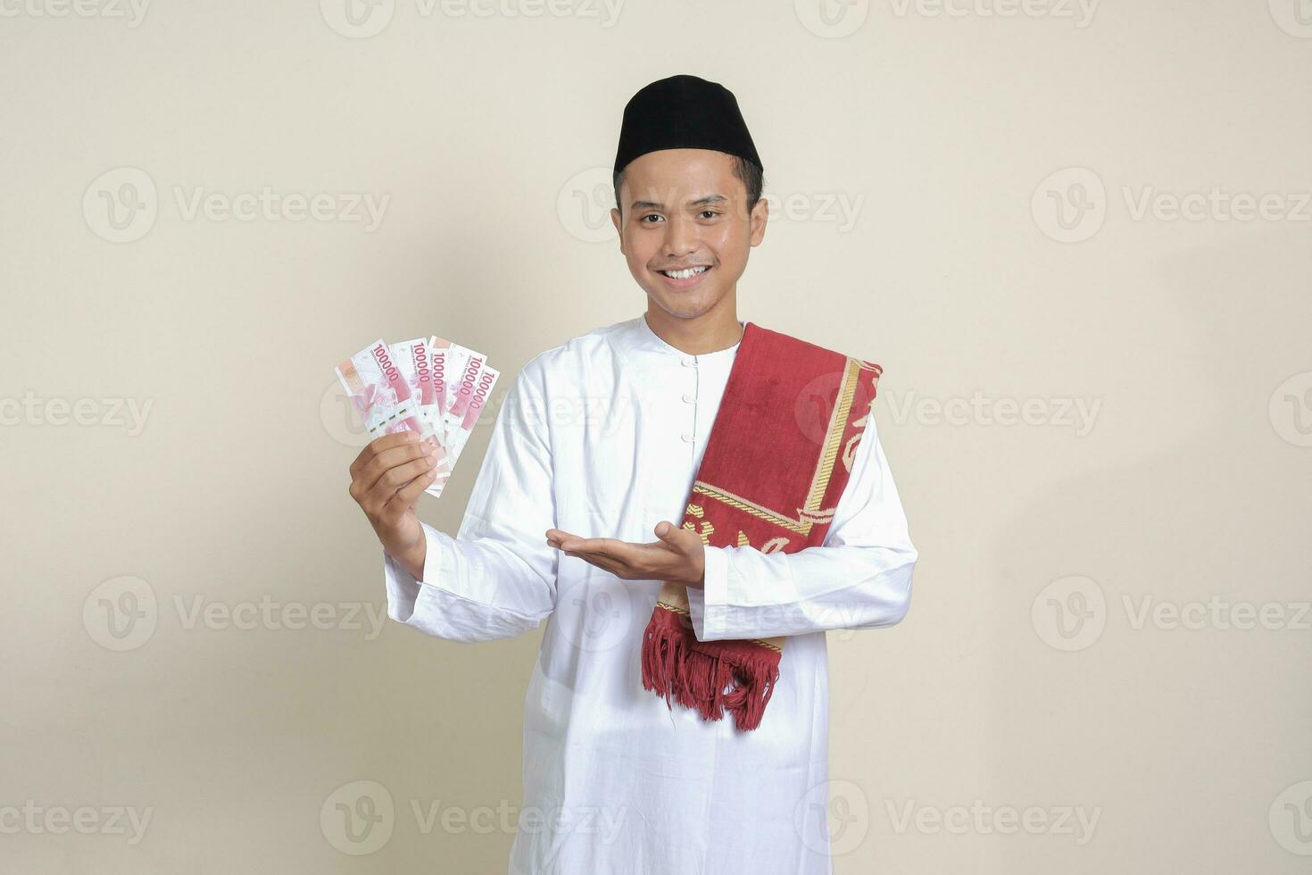 portrait de attrayant asiatique musulman homme dans blanc chemise montrant un cent mille Rupiah tandis que montrer du doigt à le côté. financier et des économies concept. isolé image sur gris Contexte photo